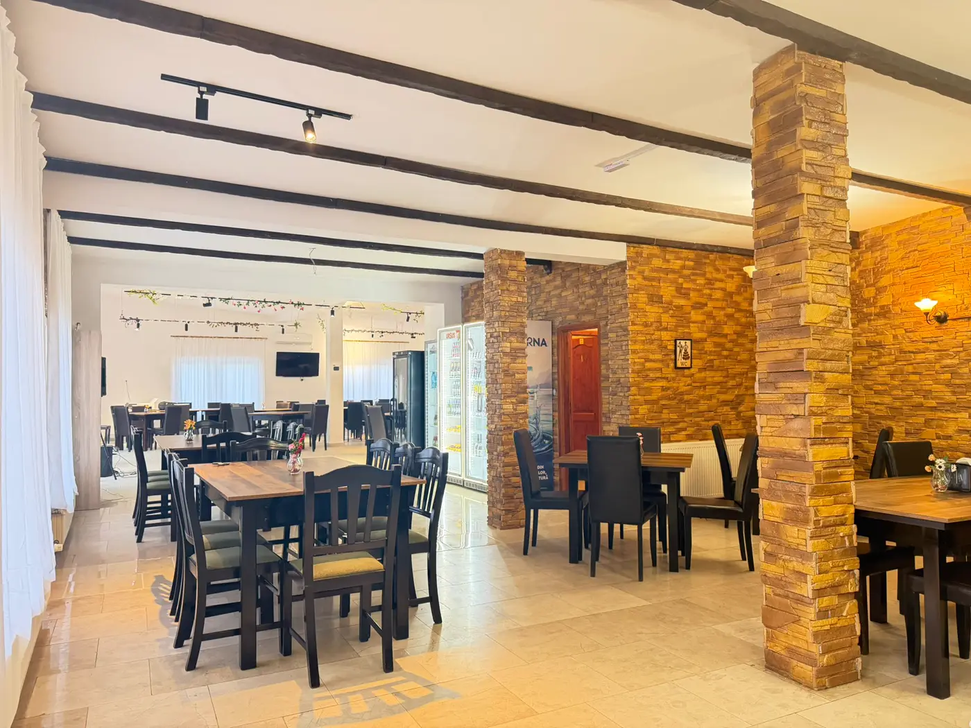 Sala interioară de la Batiz, cu grinzi de lemn, pereți de piatră și mese lungi